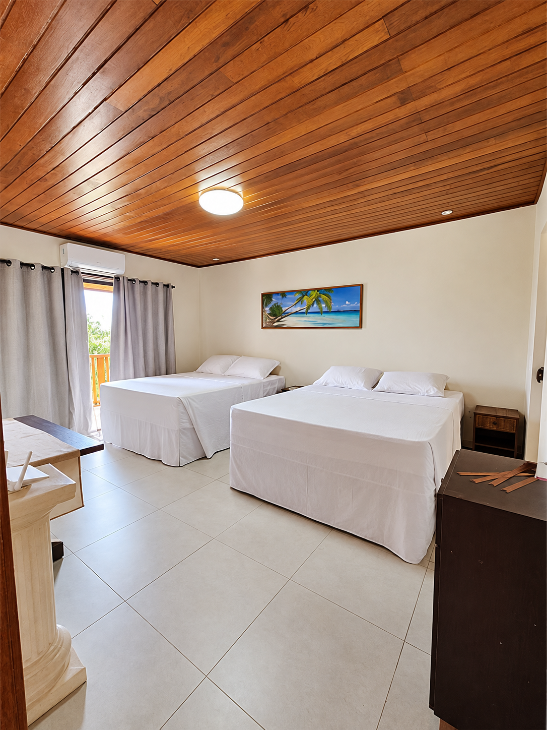 Quarto com duas camas, roupa de cama clara e teto de madeira